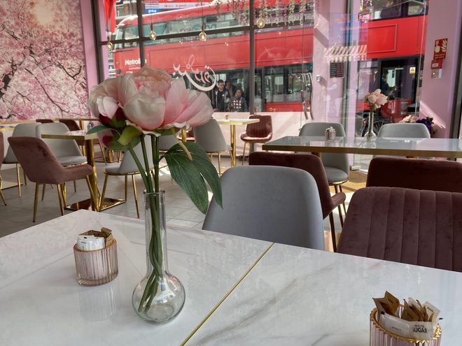 A marble table with a single pink peony in a glass vase and velvet chairs receding towards the front window.