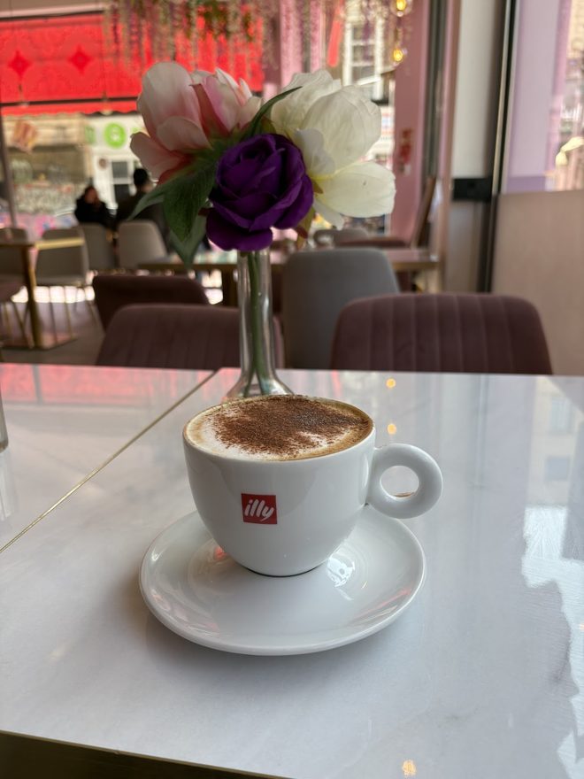 A cappuccino on the table with the pink interior behind.
