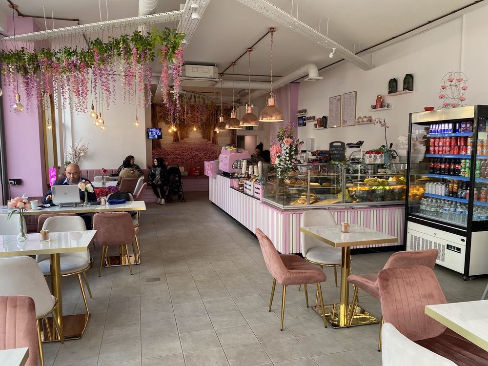 The pink interior of BeitAlawared Cafe on Kilburn High Road, with a hanging blossom ceiling, pastry counter and tables down the room.