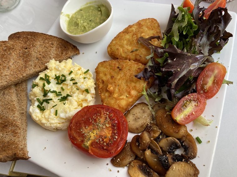 A plate of scrambled eggs with pitta, hash browns, mushrooms, tomato and green dip.